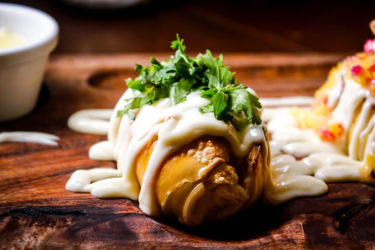 Delicious stuffed pastry topped with creamy sauce and fresh herbs on a wooden board.